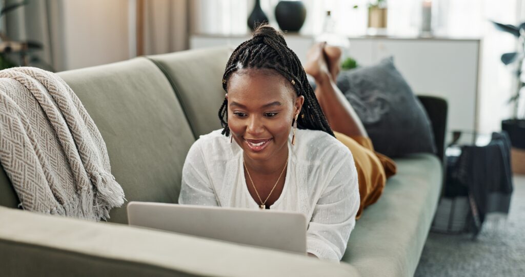 Black woman on sofa, relax or typing on laptop for remote work, social media or blog post research