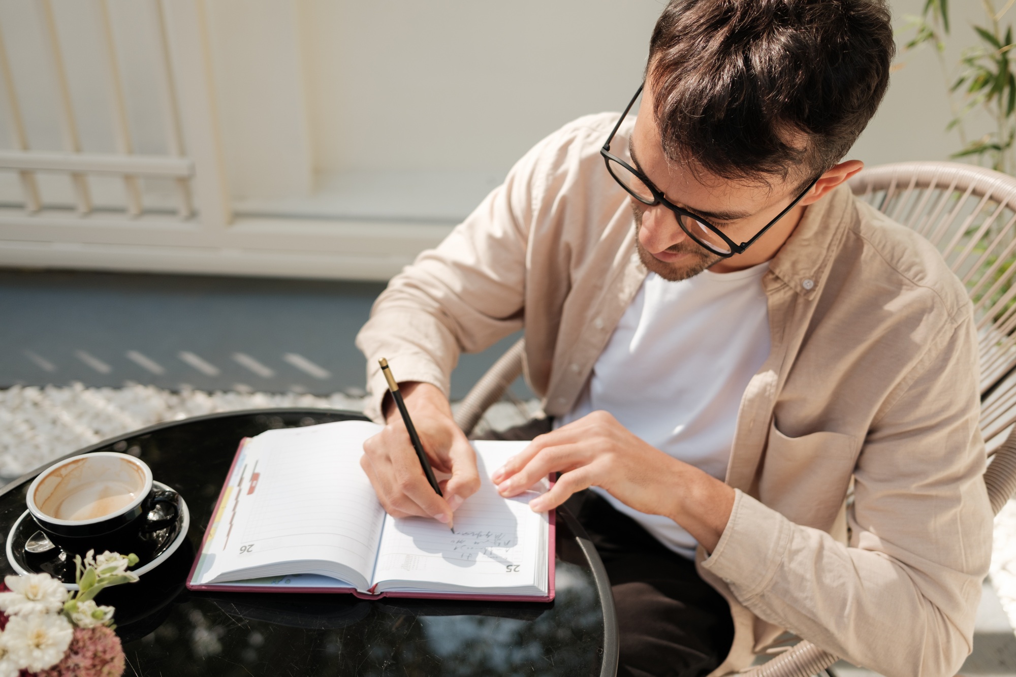 Man writing in a journal outdoors with coffee